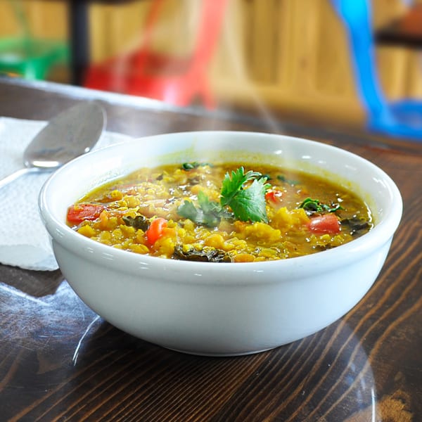 Steaming bowl of Zest Kitchen's vegan lentil soup with tomatoes and cilantro on a wooden table.