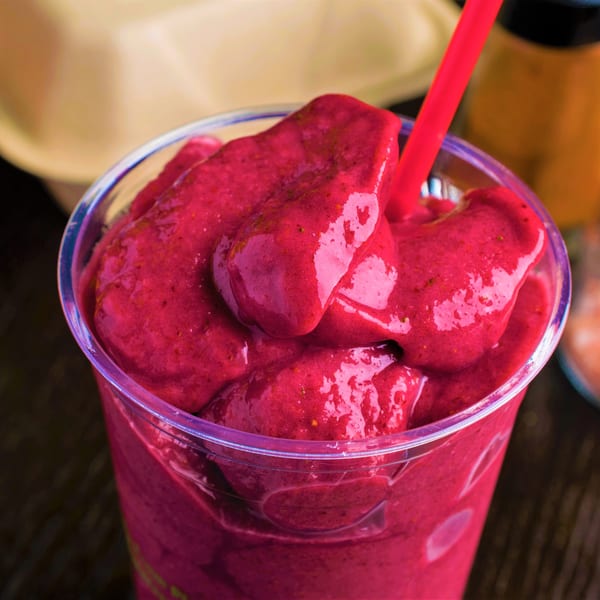 Close-up of a vibrant red vegan smoothie with a red straw in a clear plastic cup.
