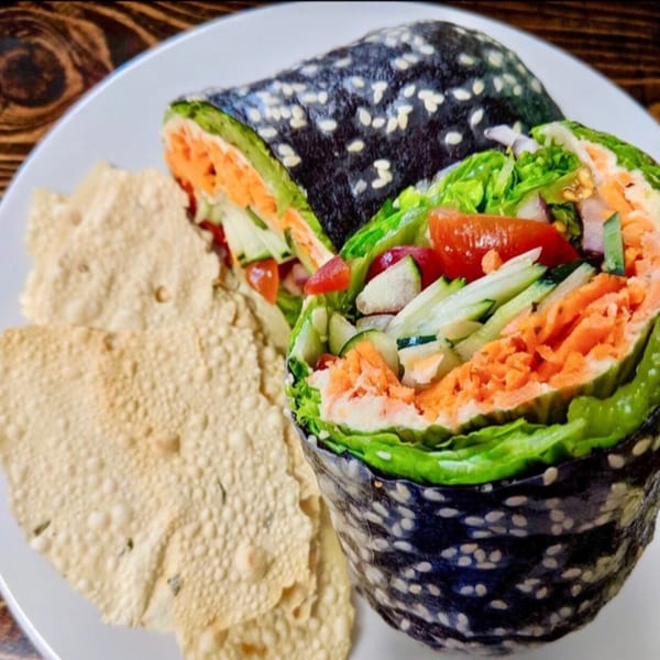A vegan nori wrap with colorful vegetables and papadum on a white plate.