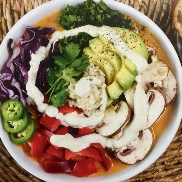 A colorful vegan bowl with red cabbage, kale, avocado, mushrooms, red peppers, jalapenos, and rice.