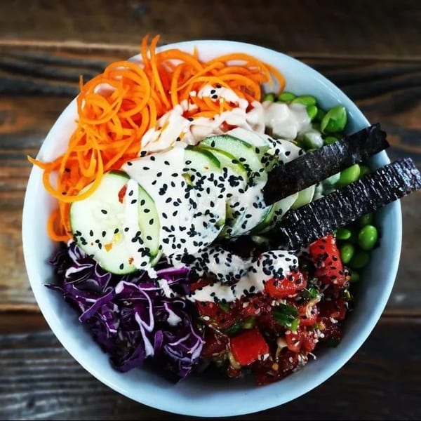 A vibrant vegan poke bowl from Zest Kitchen, featuring colorful vegetables, sauces, and seeds.